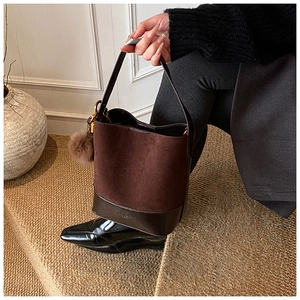 Detail of dark brown suede bucket bag with plush pom-pom and metallic logo embossing