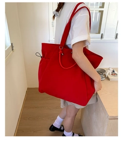 Large red canvas tote bag shown on shoulder with drawstring detail and minimalist design