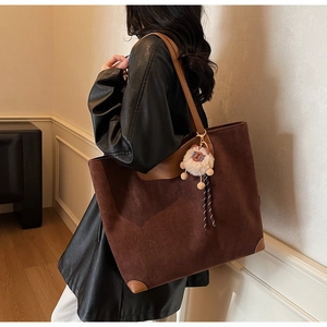 Gros plan du sac cabas en daim marron avec coins en cuir et un charm ours en peluche