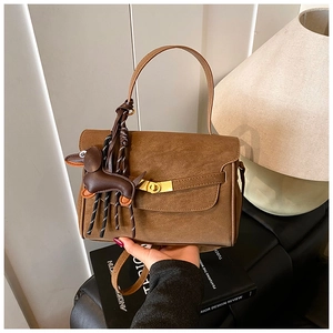 Close-up of brown matte leather shoulder bag featuring gold clasp and dachshund charm