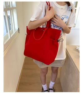 Detail of red canvas tote bag showing side drawstring pockets and thick rope handles
