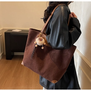 Détail d'un cabas en daim marron avec un charme lion en peluche et coins en cuir renforcé