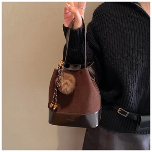Detail of suede bucket bag bottom with embossed logo and decorative plush pom-pom charm