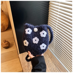 Detail of navy blue plush bucket bag with white floral embroidery and soft pom-pom charm