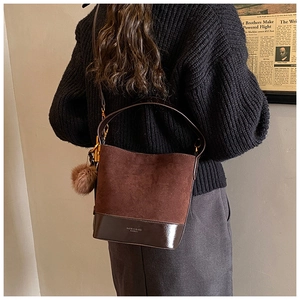 Detail view of a vintage dark brown suede bucket bag with a fuzzy ball charm on model