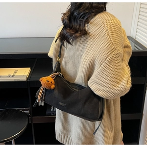 Détail du sac bandoulière en daim noir avec breloque ours et pompon tressé élégant