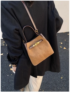 Detail of brown suede bucket bag with gold clasp and leather strap on autumn ground