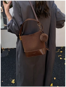 Close-up of brown suede bucket bag with plush ball charm and gold logo detail