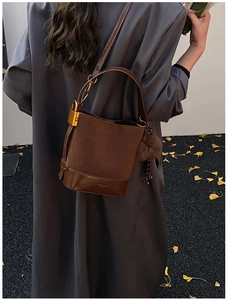 Detail of dark brown suede bucket bag with gold lock and plush charm on grey coat