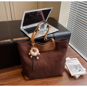 Détail d'un sac cabas en daim marron avec anses en cuir et un charm de lion en peluche