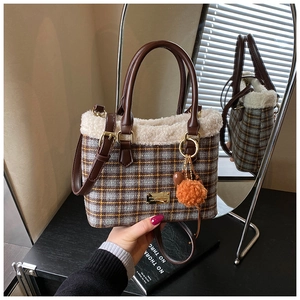 Detail of plaid bucket bag with beige faux fur trim and orange pompom accessory