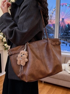 Brown suede tote bag with plush bear charm shown in a cozy winter scenery setting
