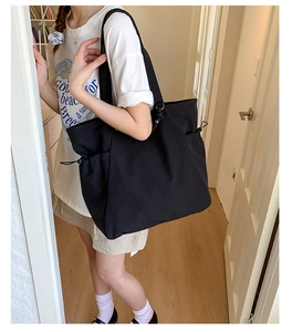 Detail view of large black tote bag with side drawstring pocket worn over the shoulder