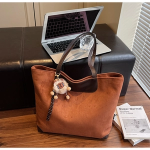 Détail d'un sac cabas en daim marron avec pendentif mouton et ordinateur sur parquet
