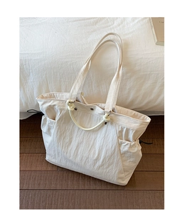 Close-up of cream nylon tote bag featuring drawstring sides and knotted ring handles
