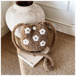 Detail of a brown plush bucket bag with white floral embroidery in a cozy setting