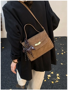 Detail of dark brown suede shoulder bag with gold hardware and dog charm in autumn scene