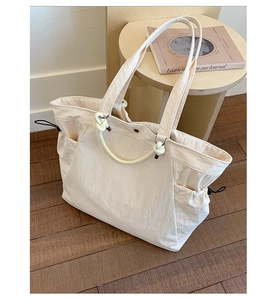 Detail of a creamy beige tote bag with drawstring side pockets on a wooden floor