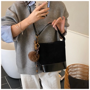 Detail of black suede bucket bag with leather base, plush charm and decorative silk scarf