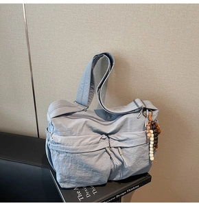 Detailaufnahme einer hellblauen Nylon-Umhängetasche mit Reißverschlusstaschen und Perlenanhänger