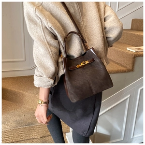Detail of dark brown bucket bag with gold turn-lock buckle and textured suede material