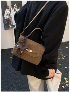Brown suede shoulder bag featuring a gold buckle clasp and a leather dog charm in autumn scene