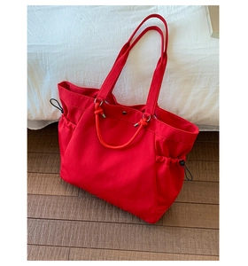 Detail of red large-capacity tote bag featuring black drawstring side closures and handles