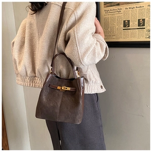 Detail of dark brown bucket bag with gold twist lock on a minimalist leather surface