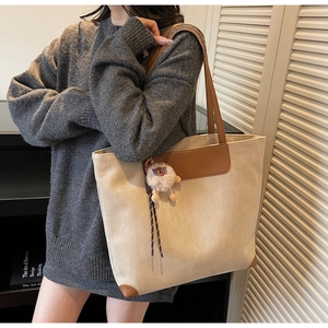 Sac cabas beige avec finitions en cuir marron et breloque mouton porté à l'épaule