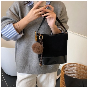 Detail of black suede and leather bucket bag with brown pompom and geometric strap