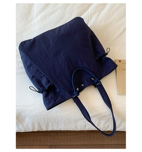 Detail view of large navy blue tote bag with drawstring sides on a clean white bed