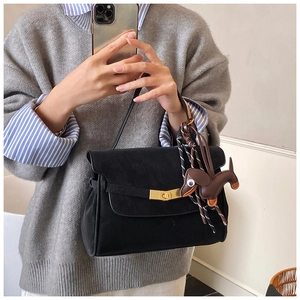 Detail view of black suede handbag with gold turn-lock and dachshund charm accessory