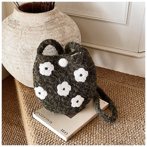 Detail of dark green plush bucket bag with white floral embroidery on a magazine