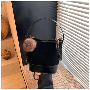 Detail of black suede bucket bag with leather stitching and a brown plush ball charm