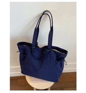 Detailed view of dark blue tote bag with functional side drawstrings on a white stool