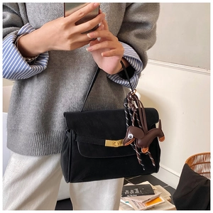 Detail of black satchel bag with golden clasp and brown dachshund charm on gray sweater