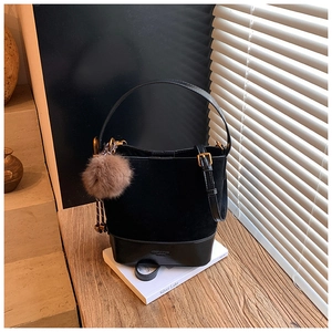 Detail of black suede bucket bag featuring polished leather base and plush brown charm