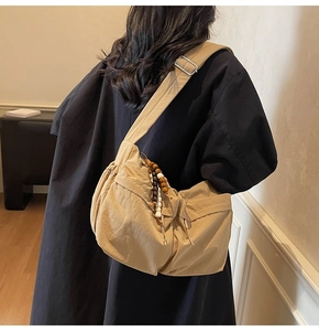 Detailaufnahme einer beigen Nylon-Umhängetasche in Halbmondform mit Holzperlen-Anhänger