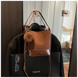 Detail of brown suede bucket bag with leather trim and decorative fur ball charm