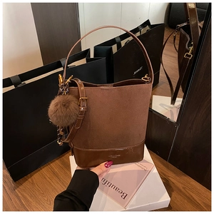 Detail of brown faux suede bucket bag with adjustable strap and decorative fur pompom charm