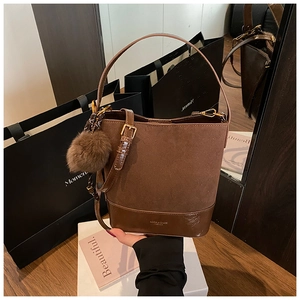 Close-up of dark brown suede bucket bag with leather patchwork and golden hardware
