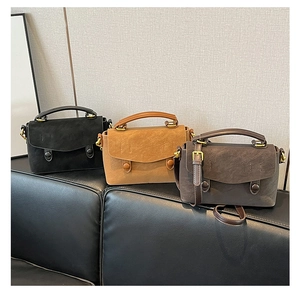 Three vintage style crossbody bags in black, camel and brown on a leather sofa