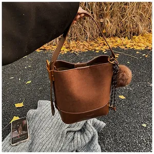 Detail of a brown suede bucket bag with decorative pompom and woven cord detail
