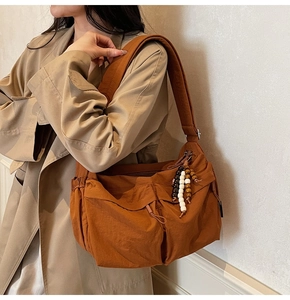 Detail der karamellbraunen Umhängetasche aus Nylon mit Taschen und Holzperlen-Anhänger