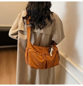 Detail der orangefarbenen Kuriertasche mit mehreren Taschen und Holzperlen-Anhänger