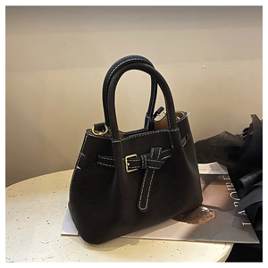 Detail of black leather handbag with white stitching and gold buckle on a marble stand