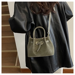 Model wearing dark olive suede bucket bag with leather strap on a minimal staircase
