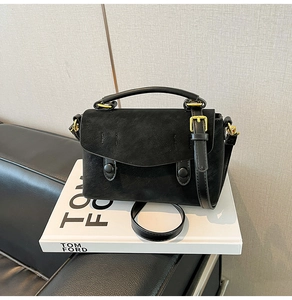 Detail of black crossbody bag with gold buckle on Tom Ford book over leather sofa