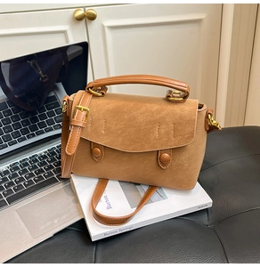 Detail of camel suede shoulder bag with golden buckles and stitching beside a laptop