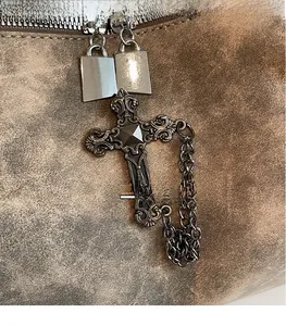 Dettaglio borsa vintage in pelle marrone con doppia cerniera e ciondolo a croce metallica